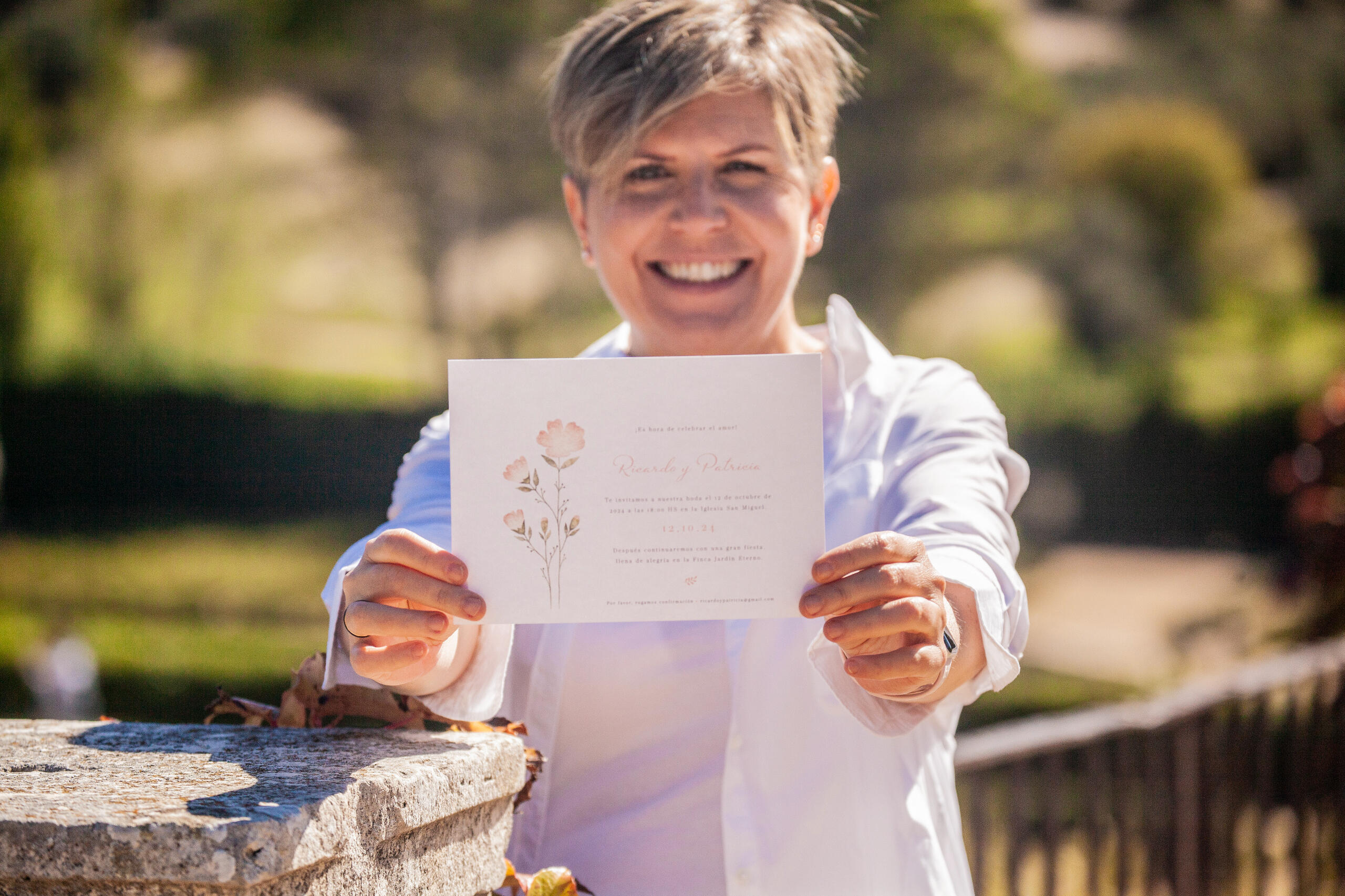 Invitación Coral Enseño la invitación Coral que contiene ilustraciones de flores en color coral y verde. Se muestra un paisaje verde detrás de mi.